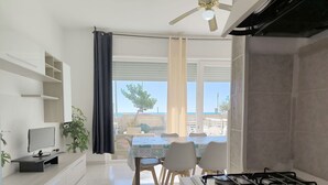 Une cuisine moderne équipée d’une cuisinière à gaz, un coin repas avec une table et des chaises, et une vue sur la mer grâce à de grandes fenêtres.
