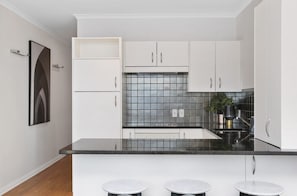Una cocina moderna con armarios blancos, encimera negra y salpicadero de azulejos.