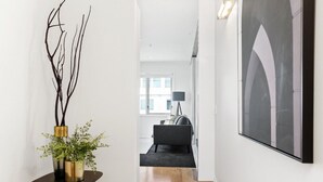 Un passadís amb un disseny interior modern, que inclou una taula rodona fosca amb una planta, un sofà negre i una catifa gris, i una obra d'art gran emmarcada a la paret.