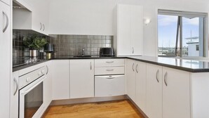 Una cuina moderna amb armaris blancs, taulell negre, forn integrat i vista al port esportiu a través d'una finestra gran.