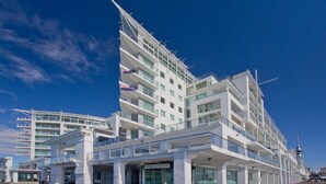 Un hotel modern d'àmbit superior amb una façana blanca destacada, múltiples balcons i un cel clar al fons.