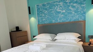 A neatly made bed with white linens, a wooden headboard, and a wall mural of water.