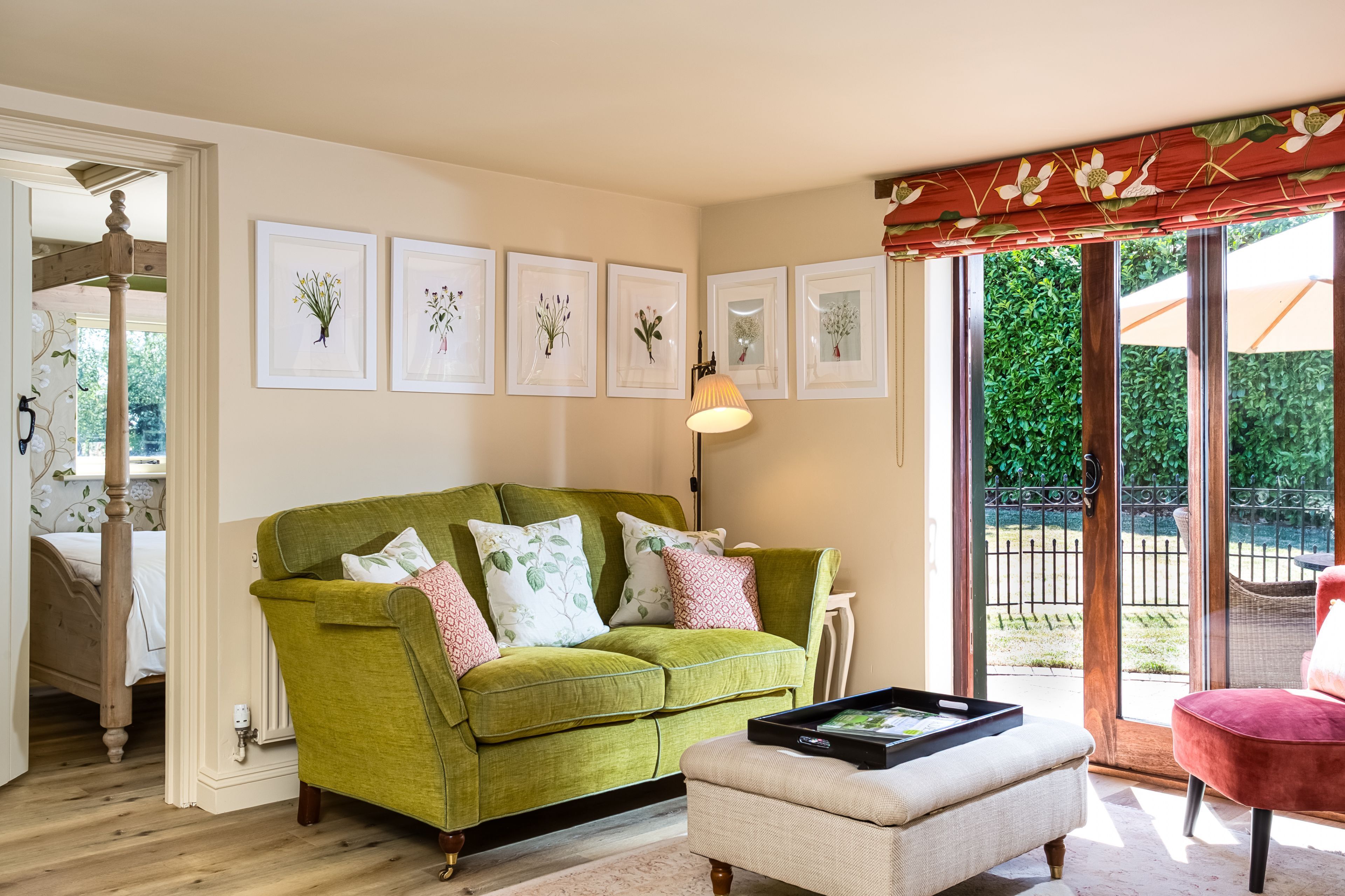 Een woonkamer met een groene bank, een witte fauteuil en een salontafel. Op de muur hangen botanische prints in lijsten en er is een groot raam met uitzicht op groen.