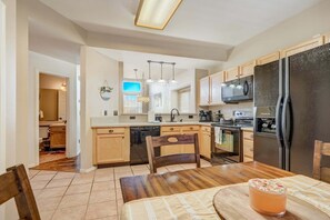 A modern kitchen with wooden cabinets, a black refrigerator, and a dining area with a table and chairs. - 4286 Morning Glory (Colorado Springs)