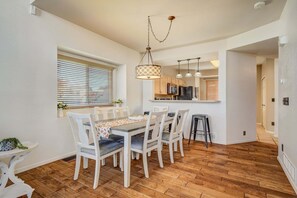 A dining area with a wooden table, white chairs, and a hanging light fixture. - 4286 Morning Glory (Colorado Springs)