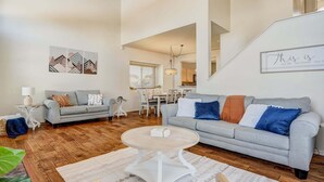 Ein geräumiges Wohnzimmer mit grauem Sofa, einem runden Couchtisch und einem Essbereich im Hintergrund.