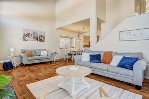 A spacious living room with a grey sofa, a round coffee table, and a dining area in the background. - 4286 Morning Glory (Colorado Springs)