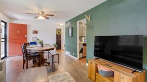 Un comedor con una mesa y sillas de madera, un ventilador de techo y un televisor sobre un mueble de madera.