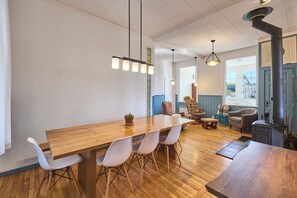 Een moderne eetruimte met een houten tafel, witte stoelen, hanglampen en een houtkachel.
