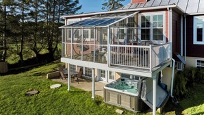 Una casa de dos pisos con un balcón acristalado, un jacuzzi y un patio.