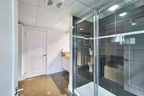Een badkamer met een douchecabine van glas, een witte deur en een betegelde vloer.