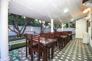 A covered outdoor dining area with wooden tables and chairs, a patterned floor, and a white ceiling with a grid pattern. - Yala Elegant Hotel (Tissamaharama)