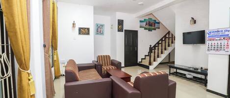 A living room with a sofa set, a TV, and a staircase.