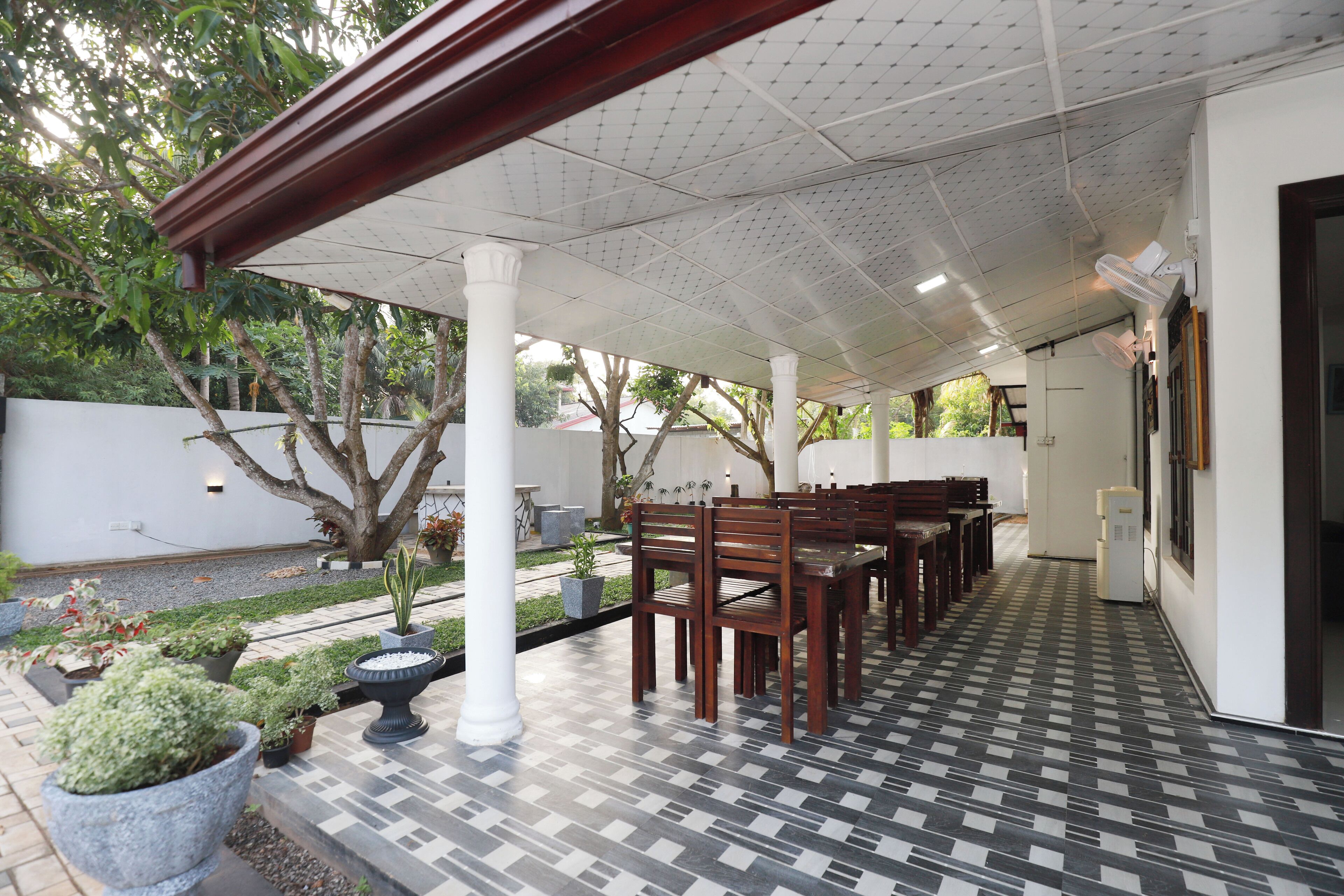 A covered patio area with tiled flooring, wooden chairs, and potted plants.