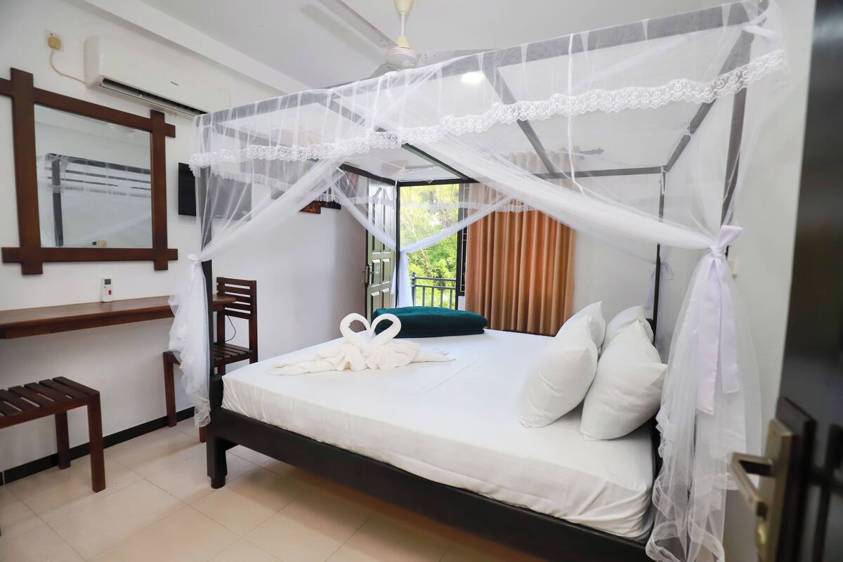 Une chambre d’hôtel avec un lit, un bureau, une chaise et une fenêtre avec des rideaux.