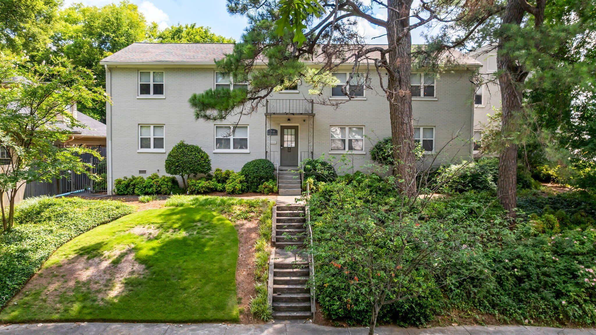 A two-story residential building with a front entrance, a small front yard, and a staircase leading to the entrance.