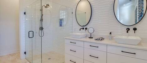 A modern bathroom with a glass-enclosed shower, white cabinetry, two sinks, and a large mirror.