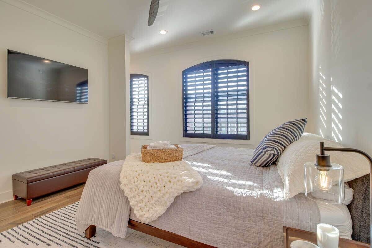 A bedroom with a bed, a bench, a TV, and large windows.