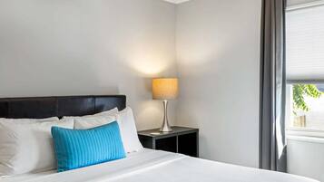 A neatly made bed with white and blue pillows, a bedside lamp, and a window with curtains.