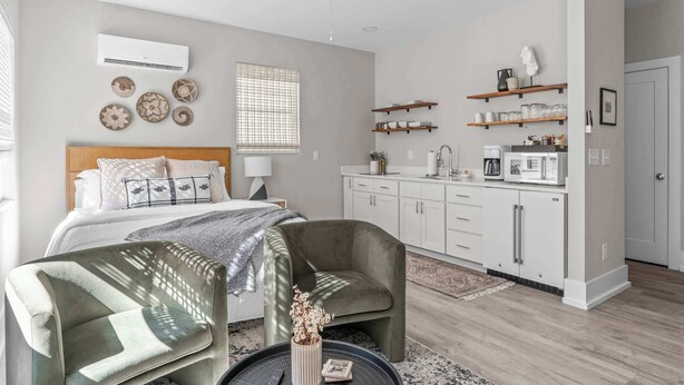 Een moderne slaapkamer met een bed, een stoel, een bureau, een kitchenette en een plafondventilator.