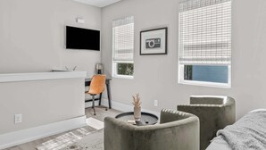 Een moderne kamer met een flatscreen televisie, een bureau, twee stoelen, een ronde tafel en een raam met zonwering.