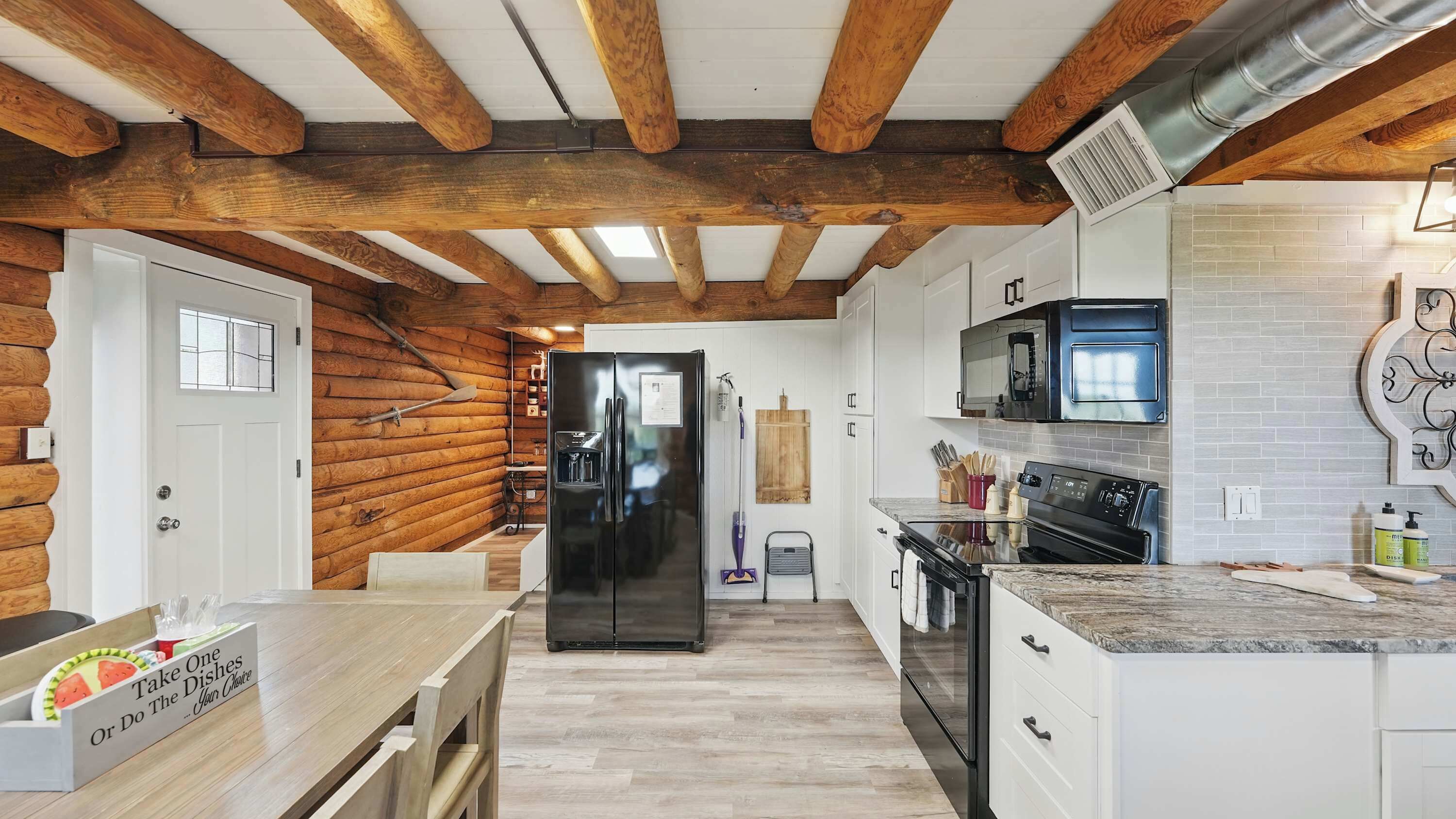 A kitchen with wooden beams, white cabinets, a black refrigerator, and a microwave.
