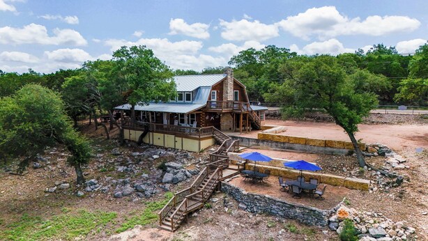 A rustic cabin with a stone chimney, wooden deck, and outdoor seating area. - Sunshine Lakehouse at Canyon Lake (Canyon Lake)
