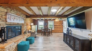 A log cabin interior with a stone fireplace, wooden dining table, and a large TV. - Sunshine Lakehouse at Canyon Lake (Canyon Lake)