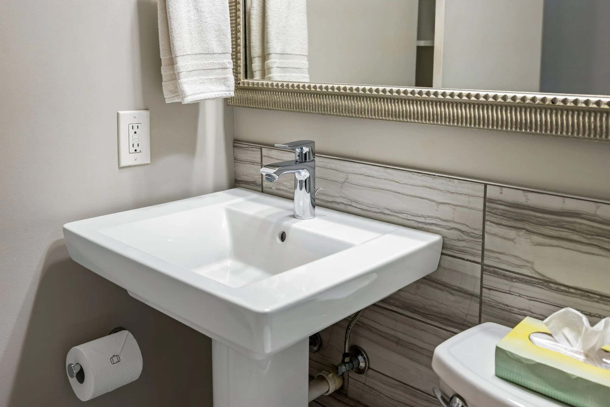 A bathroom with a white sink, a mirror with a decorative frame, and a toilet with a tissue box.