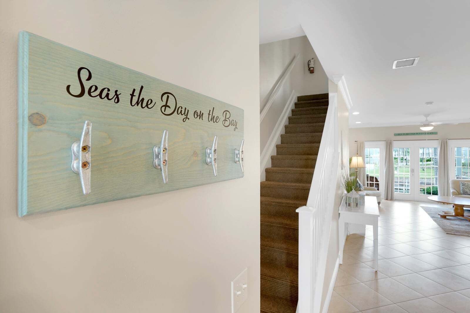 Ein Flur mit einem Holzschild mit der Aufschrift 'Seas the Day on the Bay' und einer Treppe, die zu einem Zimmer mit Blick ins Freie führt.