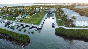 Vue aérienne d’une propriété située au bord de l’eau, avec une marina, plusieurs bâtiments blancs et une végétation luxuriante.