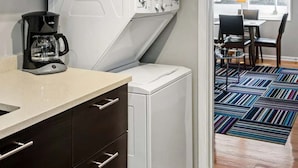 Une cuisine compacte équipée d’une machine à café, d’un lave-linge et d’un coin repas avec une table et des chaises.