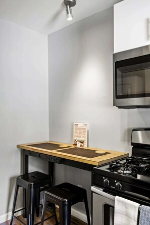 Une cuisine compacte équipée d’une cuisinière à gaz, d’un four à micro-ondes et d’un îlot central en bois avec des tabourets.