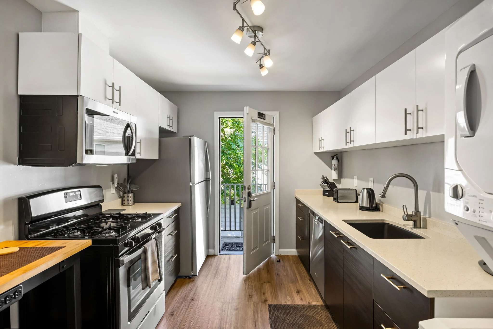 A modern kitchen with stainless steel appliances, a large window, and a door leading to a balcony.