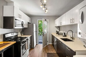A modern kitchen with stainless steel appliances, a large window, and a door leading to a balcony. - Brookwood Courtyard by BCA Furnished Apartments Bcc1b 03 C (Atlanta)