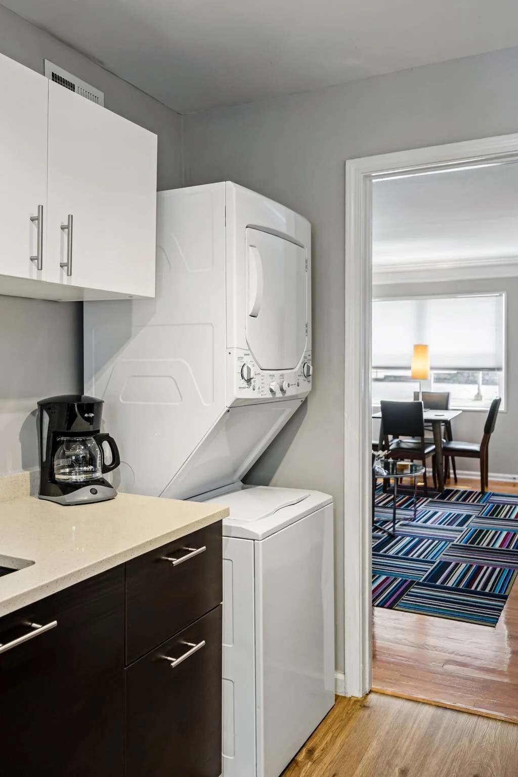 A compact kitchen with a coffee maker, a washing machine, and a dining area with a table and chairs.