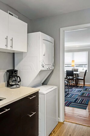 Une cuisine compacte équipée d’une machine à café, d’un lave-linge et d’un coin repas avec une table et des chaises.