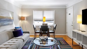 A modern living room with a sofa, a dining table with chairs, a glass coffee table, and a TV on a stand. - Brookwood Courtyard by BCA Furnished Apartments Bcc1b 03 C (Atlanta)