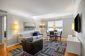 Ein modernes Wohnzimmer mit einer Couch, einem Couchtisch und einem Fernseher. Es gibt einen Essbereich mit Stühlen und einem Tisch.