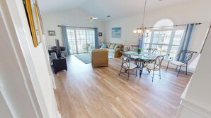 A spacious living area with a wooden floor, a sofa, a dining table with chairs, and a ceiling fan. - Magnolia Place 4781 U304 (Myrtle Beach)