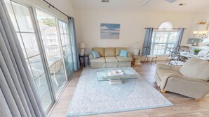 A spacious living room with a large sofa set, a glass coffee table, and a view of the outdoors through large windows. - Magnolia Place 4781 U304 (Myrtle Beach)