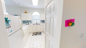 A narrow kitchen with white cabinets, a tiled backsplash, and a window with blinds. - Magnolia Place 4781 U304 (Myrtle Beach)