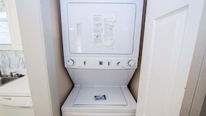 A compact, white laundry room with a front-loading washing machine and a small shelf with a detergent packet. - Magnolia Place 4709 U203 (Myrtle Beach)