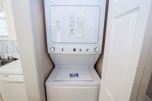 A compact, white washing machine in a narrow space, likely a utility room or laundry area. - Magnolia Place 4709 U203 (Myrtle Beach)