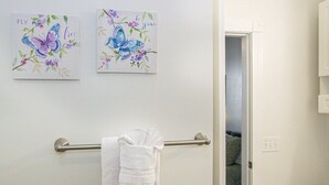 A bathroom with a towel rack holding a white towel, two butterfly-themed wall art pieces, and a partially open door leading to another room. - Magnolia Place 4709 U203 (Myrtle Beach)