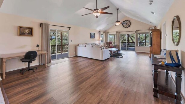 Uma sala de estar ampla com pé direito alto, piso de madeira, um sofá branco, uma escrivaninha e um ventilador de teto.
