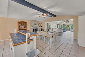 A spacious kitchen with a central island, a dining area with a white table and chairs, and a ceiling fan.