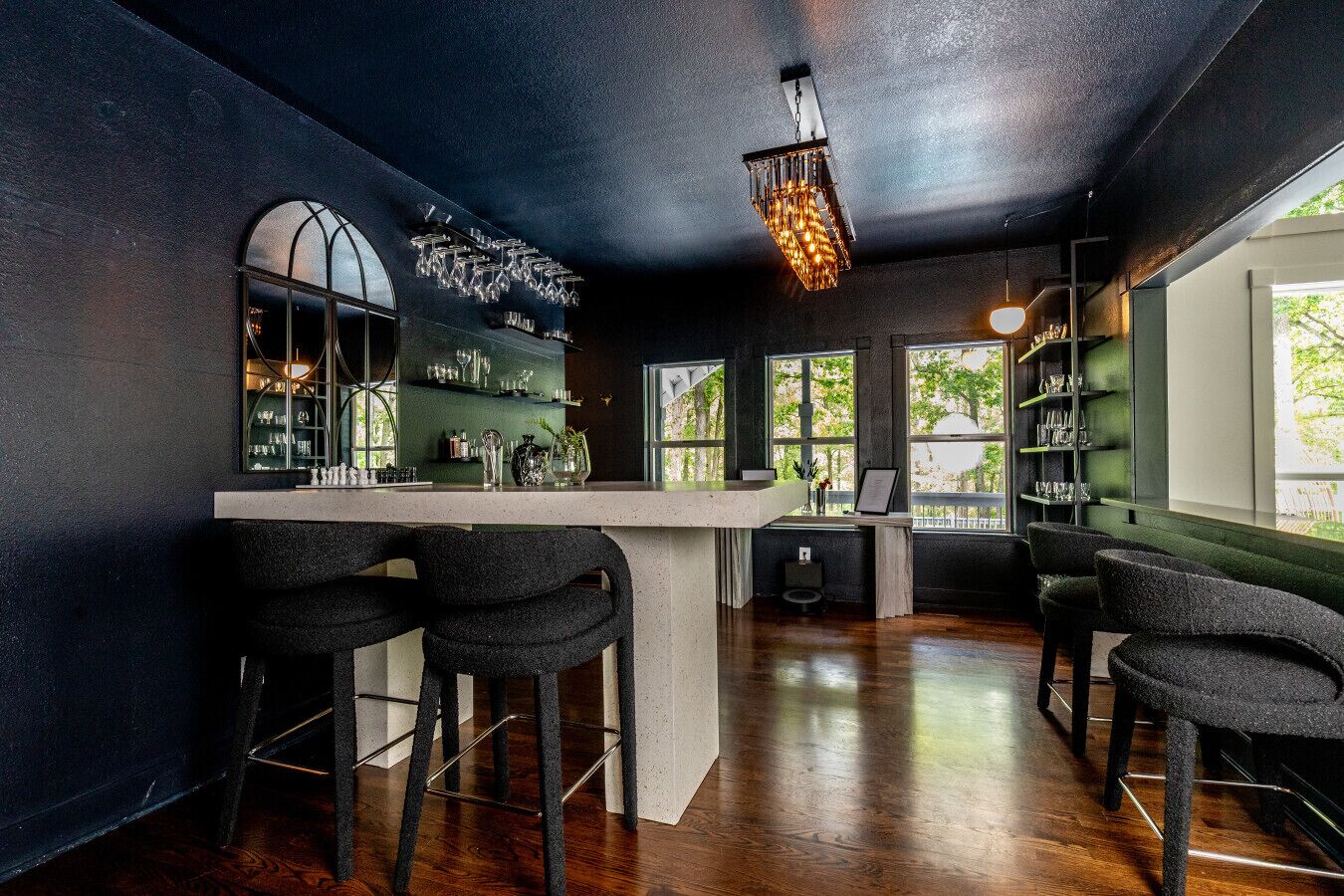A bar area with a bar counter, stools, and shelves with glasses.