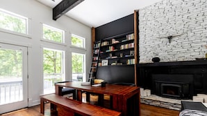 Ein modernes Wohnzimmer mit Holzesstisch, Bücherregalen, einem Kamin und großen Fenstern.