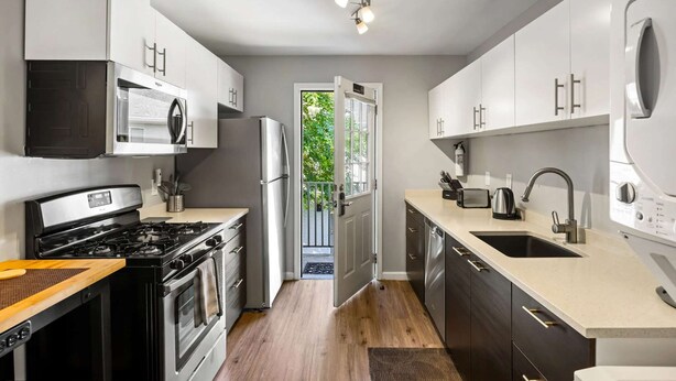 Una cocina moderna con electrodomésticos de acero inoxidable, un ventanal grande y una puerta que da a un balcón.